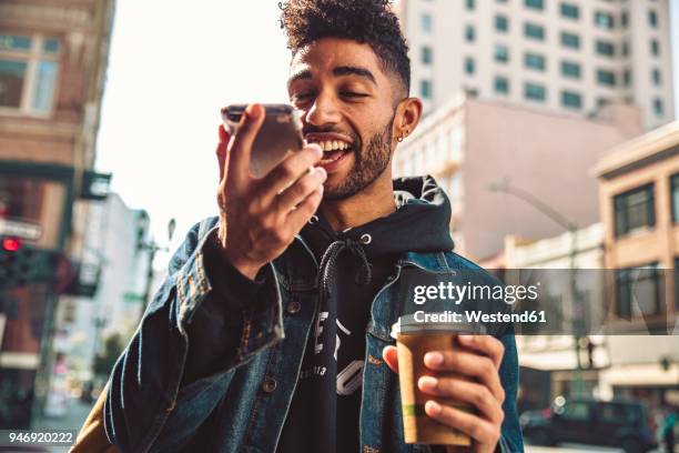 portrait of stylish young man with coffee and smartphone on the street - young men talking stock pictures, royalty-free photos & images
