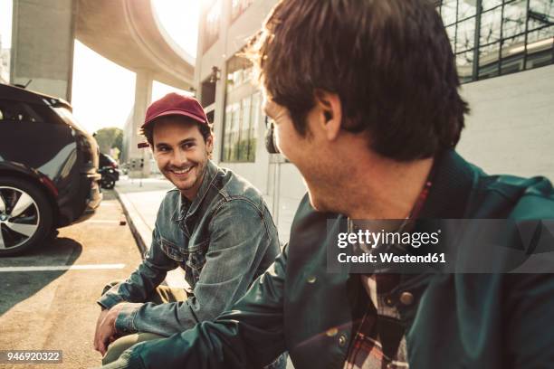 two smiling young men sitting on sidewalk - talking friends backlight stock pictures, royalty-free photos & images
