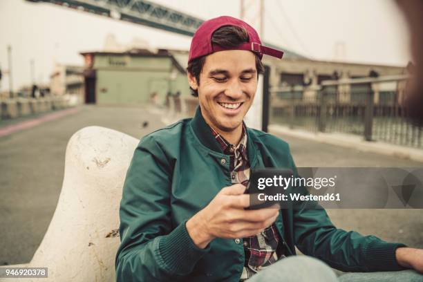 portrait of smiling young man using cell phone - chico ciudad fotografías e imágenes de stock