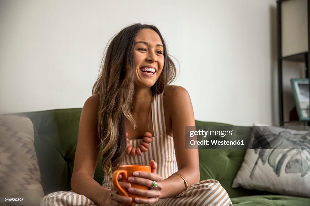 Laughing young woman with coffee mug sitting on couch