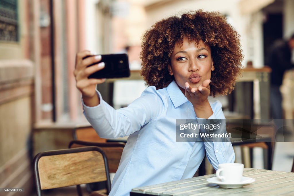 Woman with afro hairstyle sitting in outdoor cafe taking a selfie