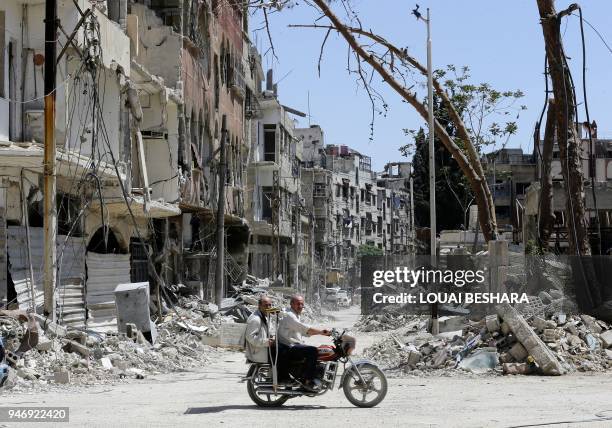 Syrians ride a motorbike along a destroyed street in Douma on the outskirts of Damascus on April 16, 2018 during an organised media tour after the...