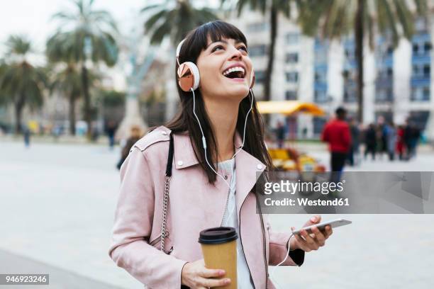 spain, barcelona, laughing woman with coffee, cell phone and headphones in the city - listening imagens e fotografias de stock