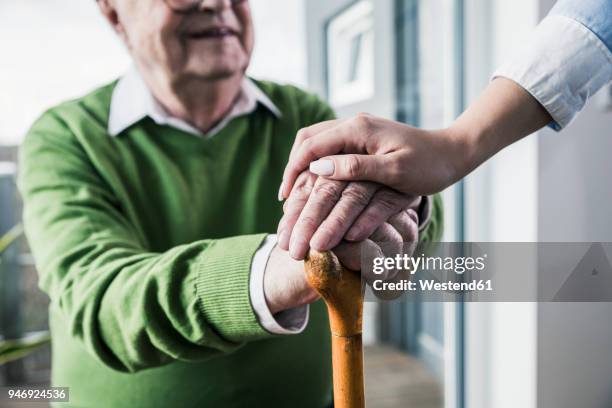 close-up of woman holding senior man's hand leaning on cane - old man young woman stockfoto's en -beelden