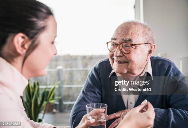 woman holding pill and glass of water for smiling senior man - old man young woman fotografías e imágenes de stock