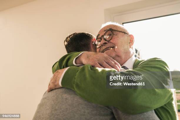 smiling senior man hugging young man - visit stock-fotos und bilder