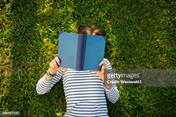 girl lying on meadow reading a book - child reading a book stockfoto's en -beelden