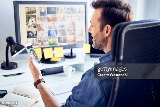 photo editor at desk in office having video chat on his phone - mobile phone edit stockfoto's en -beelden