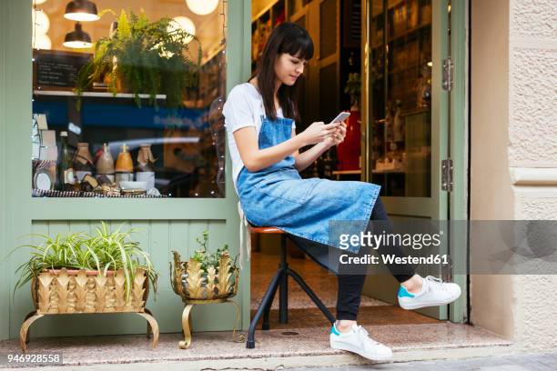 woman sitting on stool using cell phone at entrance door of a store - freelancer stockfoto's en -beelden