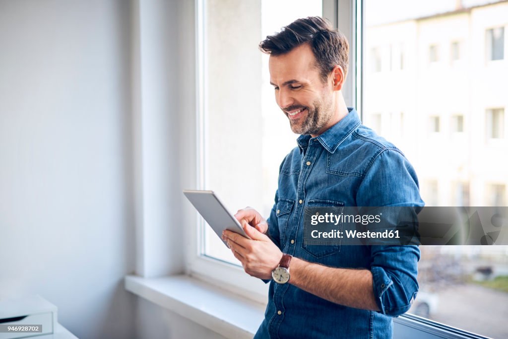 Smiling man using tablet at the window