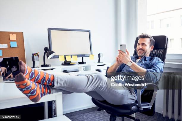 relaxed man sitting at desk in office using cell phone - feet up stock pictures, royalty-free photos & images