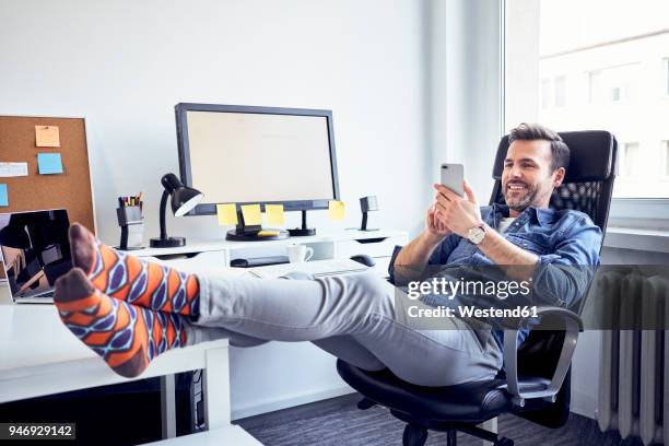 relaxed man sitting at desk in office using cell phone - de pé para cima - fotografias e filmes do acervo