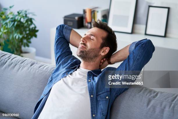 smiling relaxed man sitting on sofa daydreaming - contento foto e immagini stock