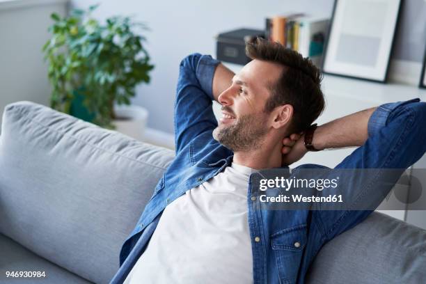 smiling relaxed man sitting on sofa looking away - hände hinter dem kopf stock-fotos und bilder