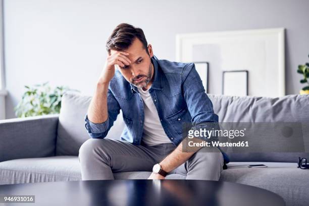 worried thoughtful man sitting on sofa - displeased 個照片及圖片檔