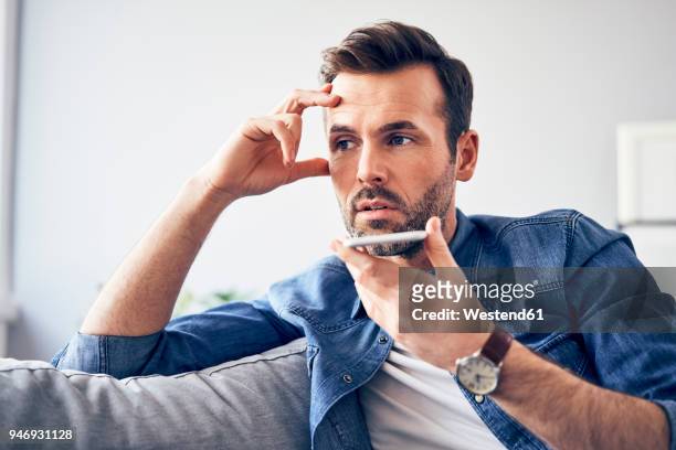 worried man sitting on sofa using cell phone - frustrated on phone stock pictures, royalty-free photos & images