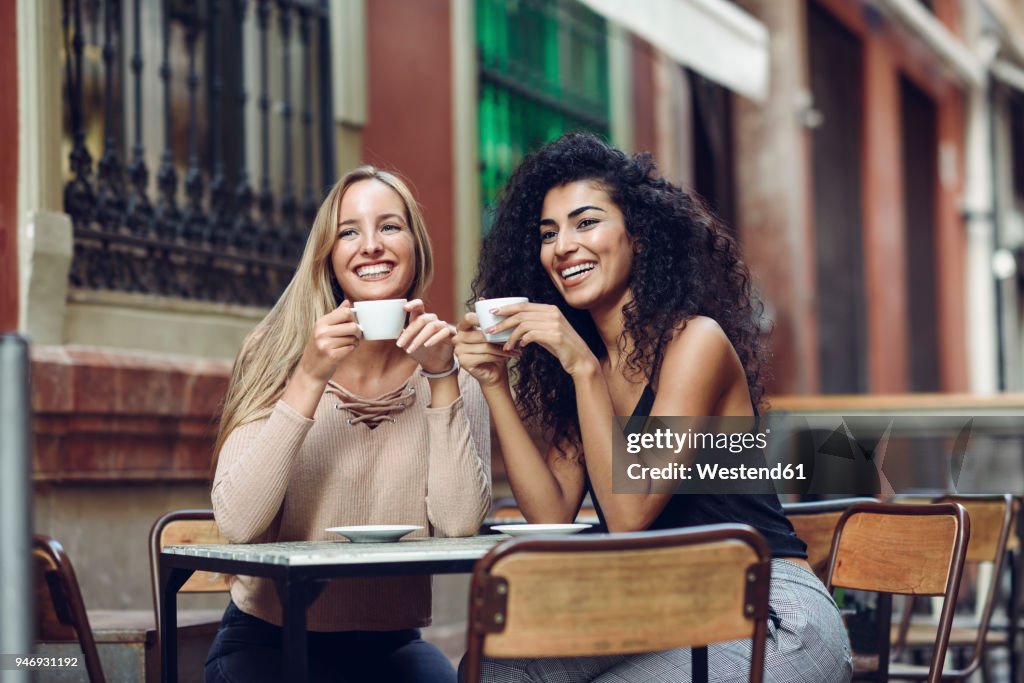 Two happy friends drinking coffee in sidewalk cafe