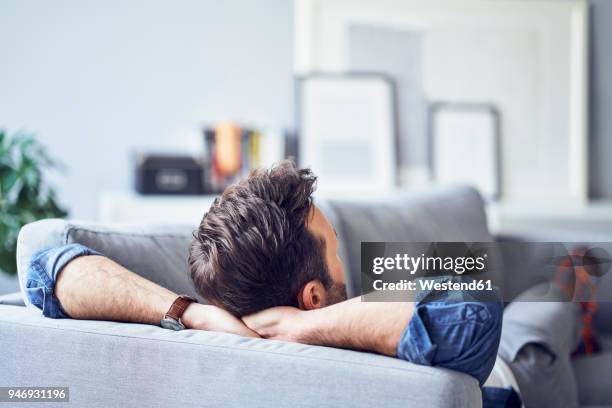 relaxed man lying on sofa - manos detrás de la cabeza fotografías e imágenes de stock