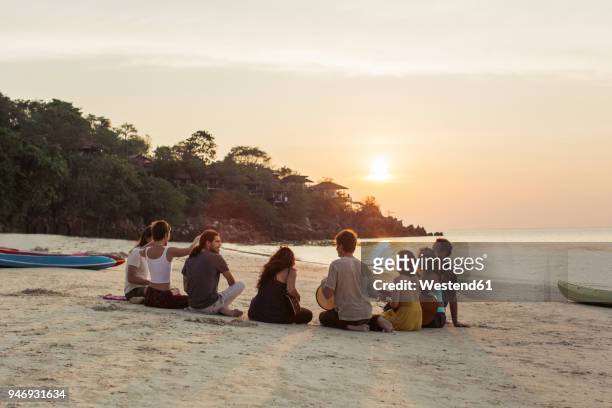 thailand, koh phangan, group of people sitting on a beach with guitar at sunset - romantic sky stock pictures, royalty-free photos & images