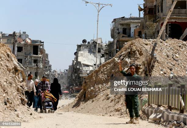 Syrian government soldier flashes the sign for victory as people walk along a destroyed street in Douma on the outskirts of Damascus on April 16,...