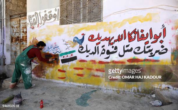 Picture taken on April 16, 2018 in the rebel-held Syrian town of Binnish shows 45-year-old Syrian artist Aziz al-Asmar drawing a graffiti, with a...