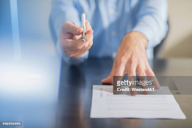 person sitting at office desk presenting ballpen and contract - dar fotografías e imágenes de stock