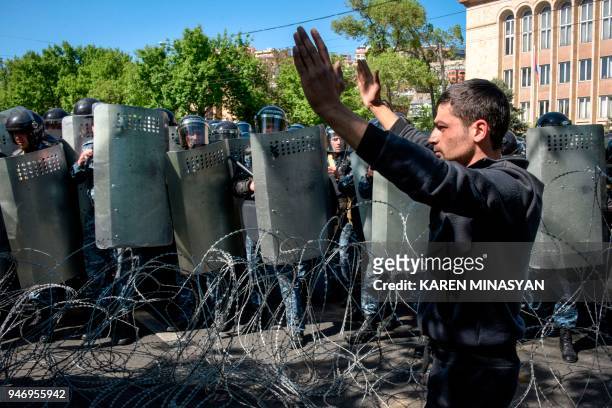 Armenian opposition supporter gestures in front of barbed wire and police officers standing guard behind their shields during a dispersal of a rally...