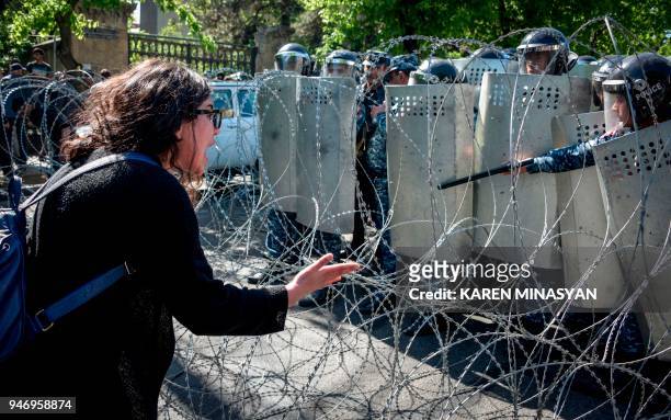 An Armenian opposition supporter gestures and shouts in front of barbed wire and police officers standing guard behind their shields during a...