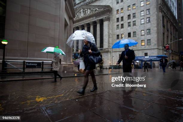 Pedestrians carrying umbrellas pass in front of the New York Stock Exchange in New York, U.S., on Monday, April 16, 2018. U.S. Stocks rallied and...