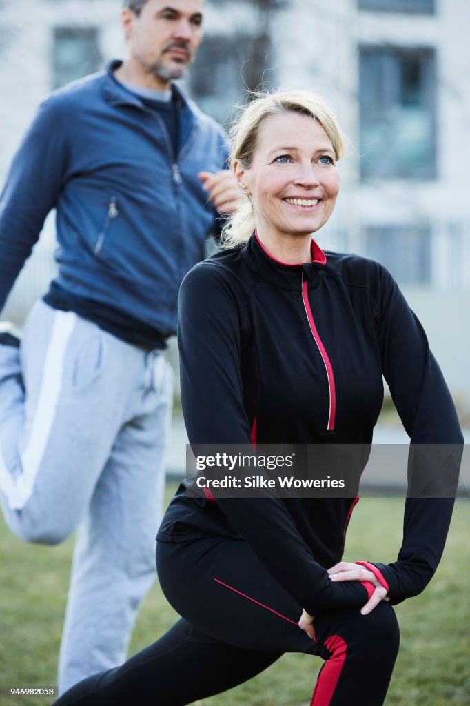 Portrait of a content mature woman and a man stretching after a run in the city