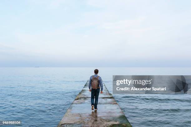 rear view of a young man with backpack walking towards the sea - weggucken stock-fotos und bilder