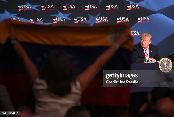 Venezuela flag is held up as U.S. President Donald Trump attends a roundtable discussion about the Republican $1.5 trillion tax cut package he...