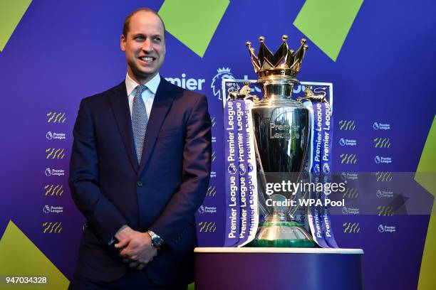 Prince William, Duke of Cambridge poses next to the English Premier League football trophy during a 'Welcome to the UK' reception on the opening day...