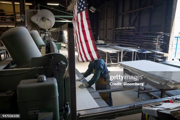 An American flag hangs as a worker operates a metal cutter at the Metal Manufacturing Co. Facility in Sacramento, California, U.S., on Thursday,...