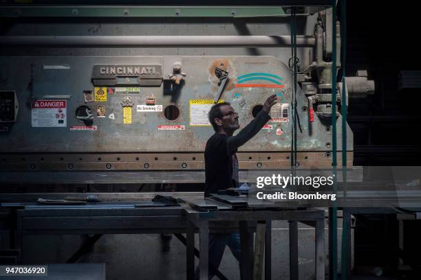 Worker reaches for a tie-down in front of a metal press brake at the Metal Manufacturing Co. Facility in Sacramento, California, U.S., on Thursday,...