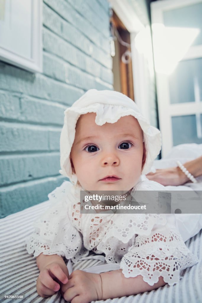 Babymädchen mit weißen Spitzenkleid auf Bauch liegend.