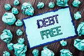 Conceptual hand writing text showing Debt Free. Concept meaning Credit Money Financial Sign Freedom From Loan Mortage written on Sticky note paper folded paper on the wooden background.