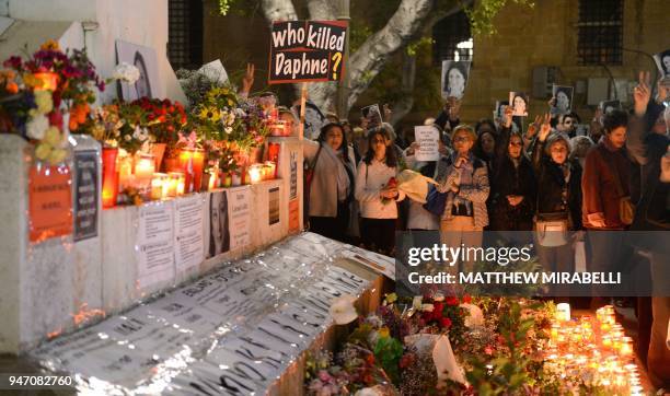 People hold portraits as they stand beside lighted candles placed in memory of murdered journalist Daphne Caruana Galizia on the sixth month...