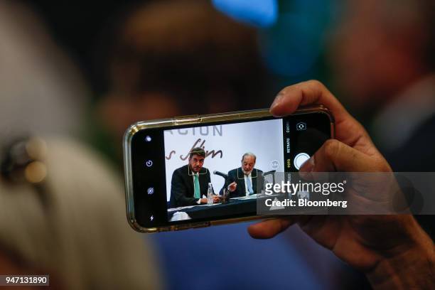 An attendee uses an Apple Inc. IPhone to take a photograph of Carlos Slim, chairman emeritus of America Movil SAB, right, speaking during a press...