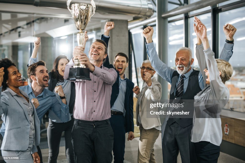 Large group of cheerful business people celebrating success with a trophy in the office.