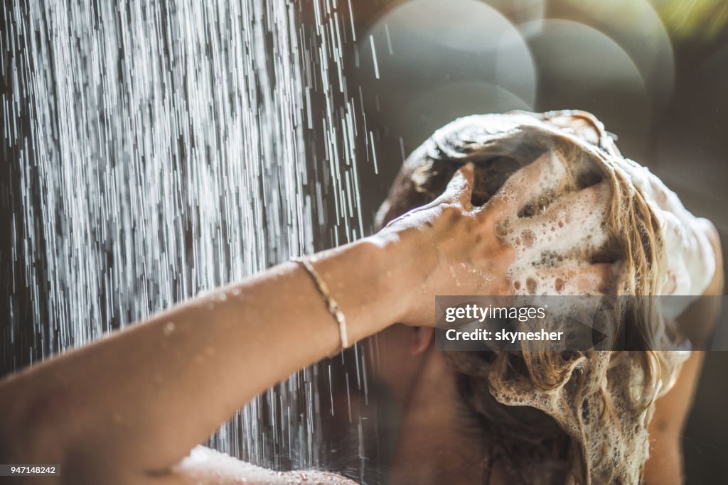 Woman washing her hair with shampoo under the shower.