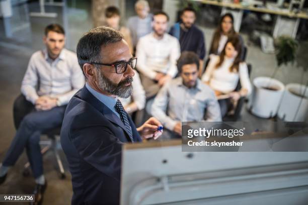 mature businessman making a plan for his colleagues on a training class. - male presenter stock pictures, royalty-free photos & images