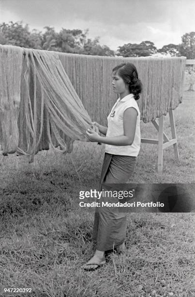 Thai girl checking a weft of hanging yards. Bangkok, 1961