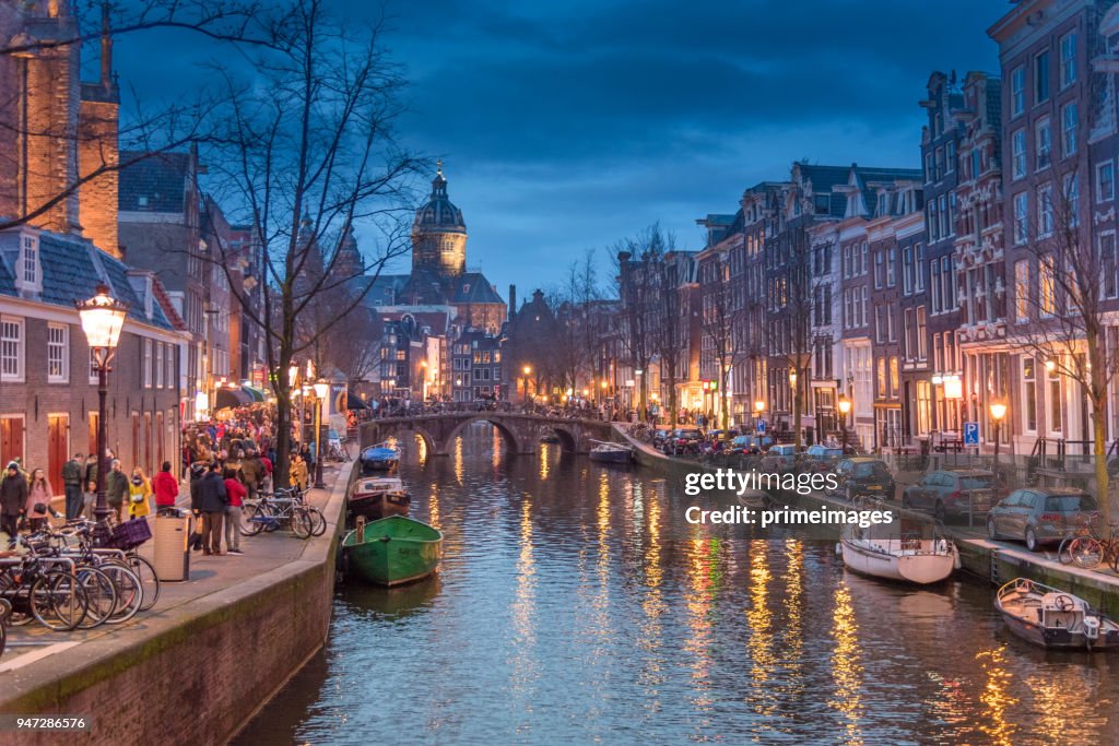 Vista do bairro de luz vermelha e canal de Amsterdam, bicicletas e ciclistas, casas flutuantes, barcos a viver. (ED.)
