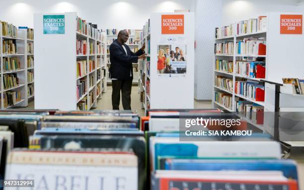 French-Ivorian writer Serge Bile looks at books as he poses at the library of the French Cultural Centre in Abidjan on March 28, 2018. - After...