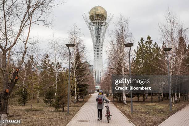 Cyclist wheels a bicycle along a path towards the Bayterak Tower in Astana, Kazakhstan, on Friday, April 13, 2018. Kazakhstan's gross domestic...