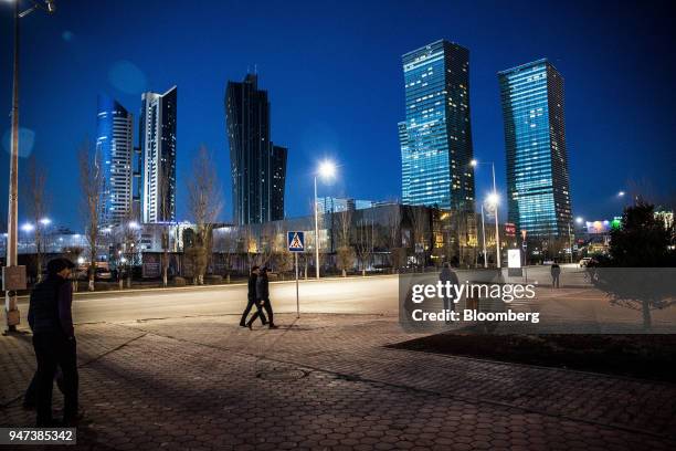 Pedestrians walk along a sidewalk near the Northern Lights towers, right, standing among other residential and commercial buildings illuminated at...