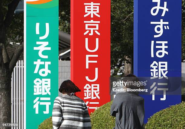 Women walk in front of signs for Mizuho Bank Ltd., right, Bank of Tokyo Mitsubishi UFJ, center, and Resona Bank Ltd. In Tokyo, Japan, on Friday, Dec....