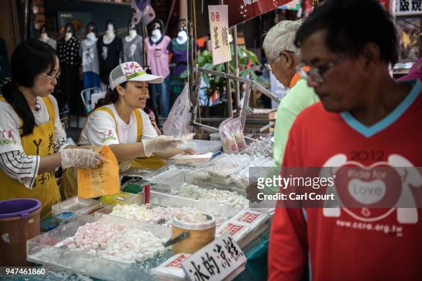 Woman serves customers at a street market while festivities take place to mark the attendance of a statue of Mazu at the nearby Xingang Fengtian...