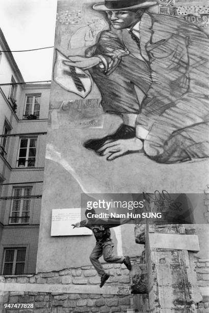 Young boy jumps from a wall in front of a gigantic graffiti. Un jeune garçon saute d'un mur devant un gigantesque graffiti.